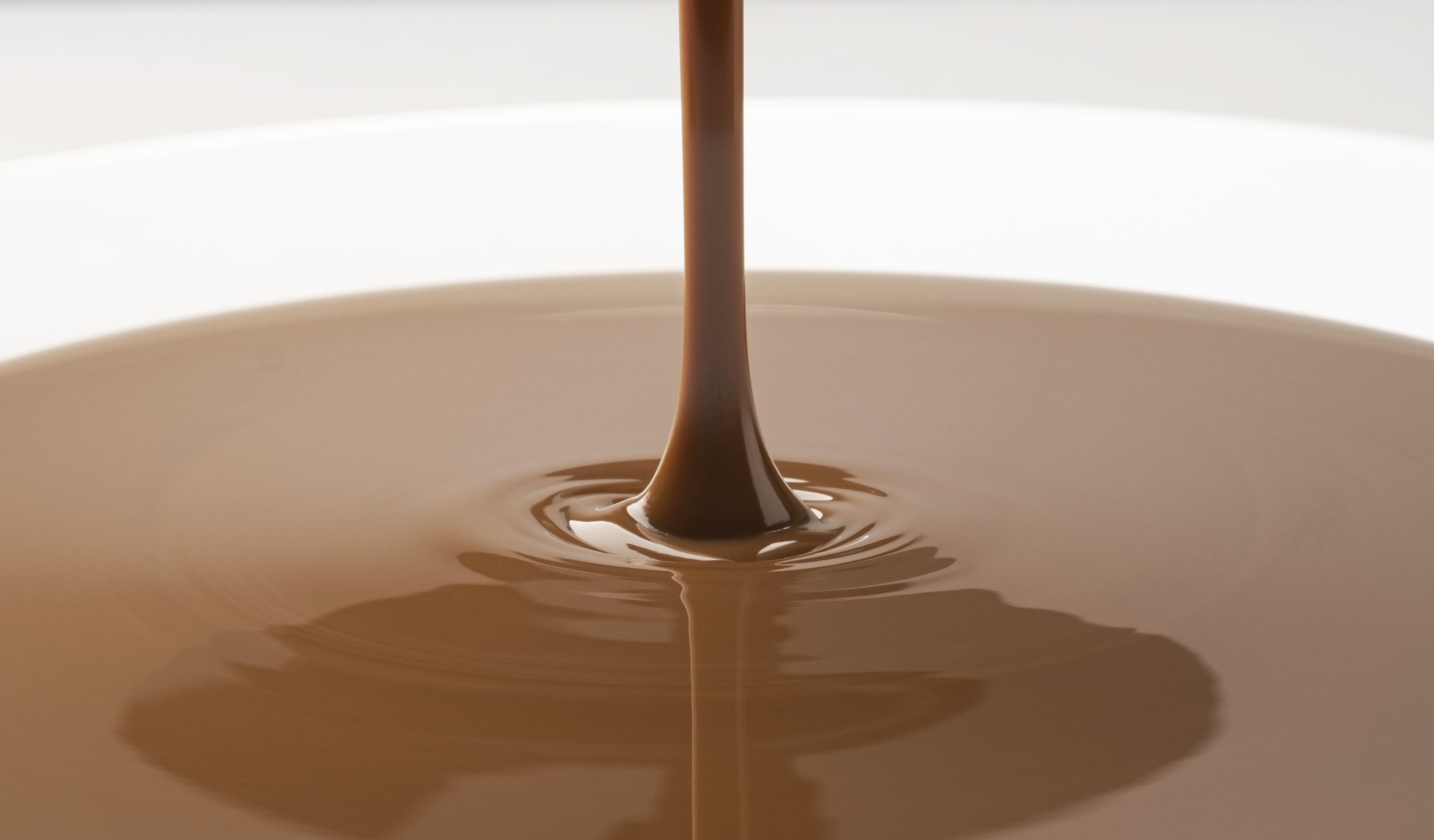 Melted dark chocolate being stirred in a bowl beside chocolate slabs and cocoa powder