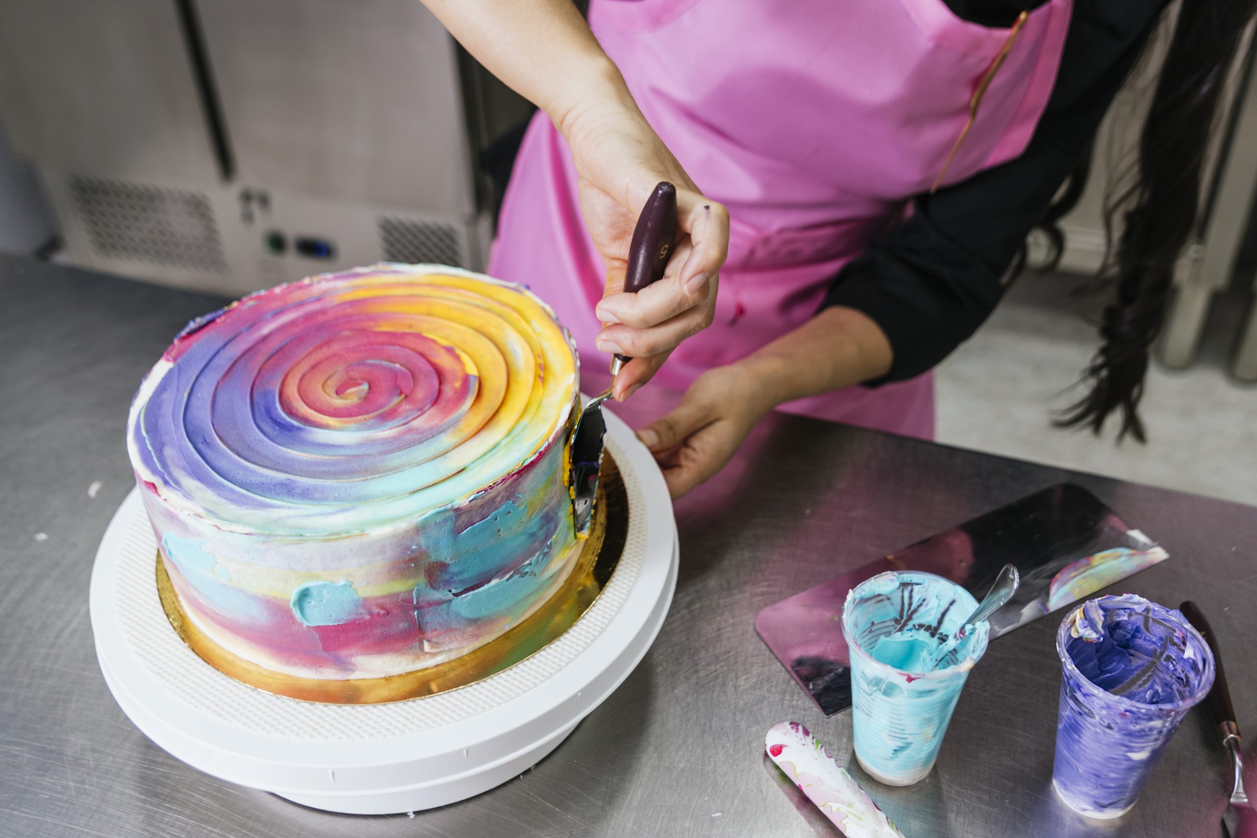 Baker smoothing white fondant over a round celebration cake with a fondant smoother